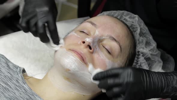 Cosmetologist Clean Clien Woman Face From Moisturizing Mask in Beauty Salon