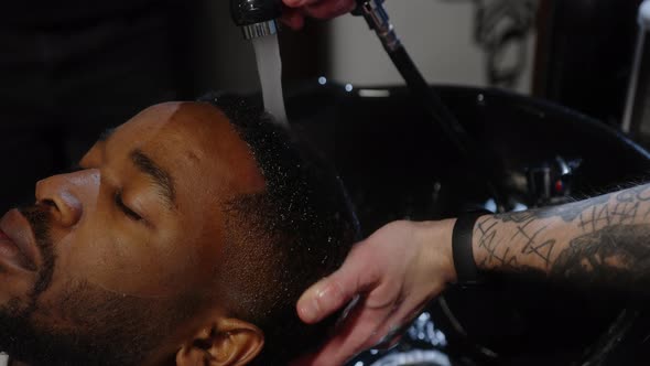 Barber Washes Shampoo Off the Head of an African American in a Special Sink