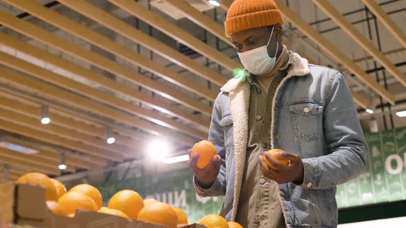 AfricanAmerican Male Shopper Wearing a Medical Mask Picks Out Fresh Oranges and Puts Them in a Bag