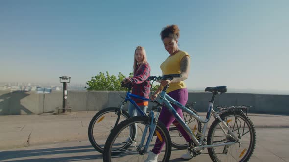 Pretty Diverse Females with Bicycles Enjoying Leisure Outdoors at Sunrise