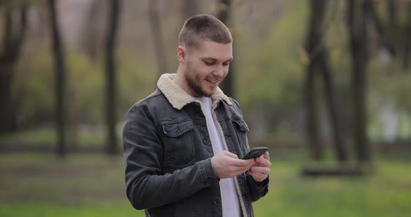 Slow Motion Smiling Man Use Smartphone Walking in the Park