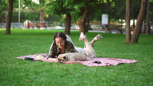 Woman with Dreadlocks Playing with Her Dog on Grass Laying on Plaid Tricking Him with a Little Snack