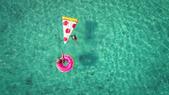 Close aerial view of two young girls swimming and playing in sea with inflatables.