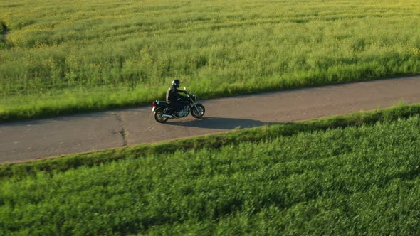 Motorcyclist Rides on Countryside Road Past Planted Field