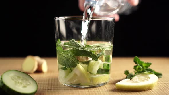 The water from the bottle pours into a glass with chopped ingredients