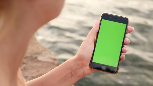 NICE, FRANCE - JULY 2017 Close-up of female with green screen display modern phone by the sea slow-m