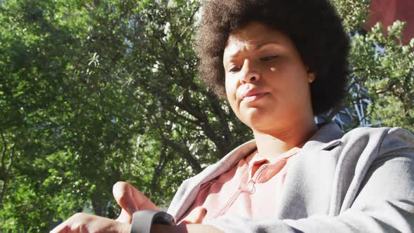 Plus size biracial woman checking smartwatch and walking in city