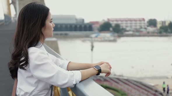 Portrait of attractive young Asian woman looking view of the river while standing on the bridge.