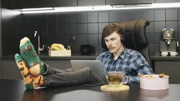 Young male in headphones listening to music and working on laptop computer from home