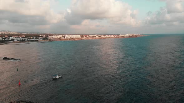 Small white fishing boat sails into open ocean with blue sky and white buildings in paphos cyprus