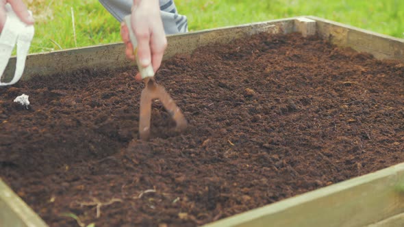 Hoeing soil in raised garden bed to sow seeds