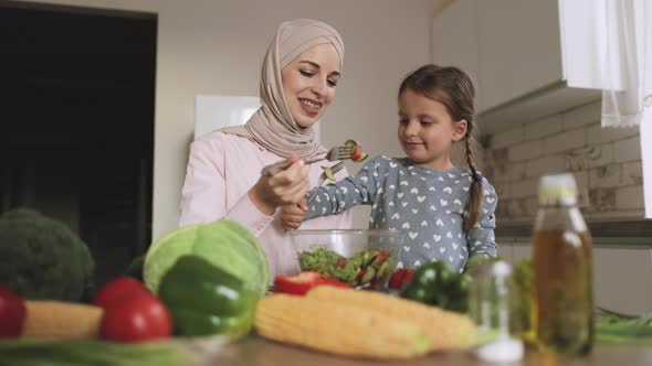 Muslim Mother Sit at Kitchen Table with Cute Preschooler Daughter Eating a Salad of Fresh Vegetables