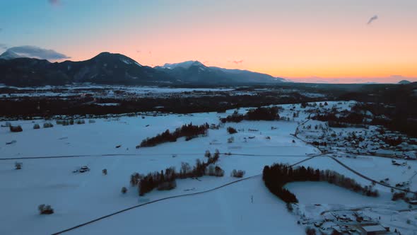 Drone shot of mountains, fields, and landscape in winter at golden hour, sunrise with snow, flying o