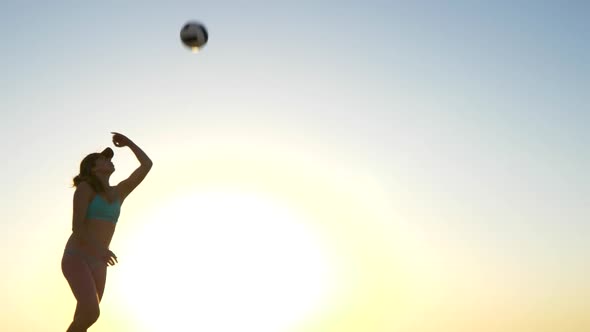 Women players play beach volleyball and a player jump serves serving the ball.