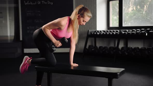 Athletic girl athlete trains her back with dumbbells in the gym. Dumbbell bench press