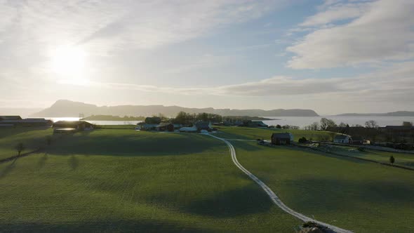 Green cultivated farm land in rural Norway next to fjord; sunset aerial