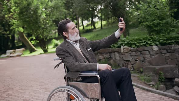 Bearded Senior Man in Wheelchair Photographing on Smartphone in Green Park