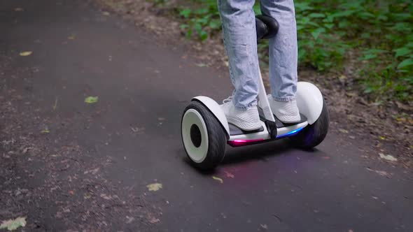 A Girl Dressed in Casual Rides Through the Forest on a Gyro Scooter. Modern Electric Transport.