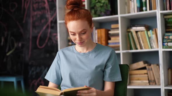 Happy Smiling Redhead Young Woman Is Reading Fascinating Book at Home in Library Room.