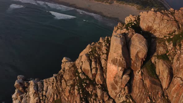 aerial top down view above Morro Bay Rock during sunset in California revealing the ocean waves cras