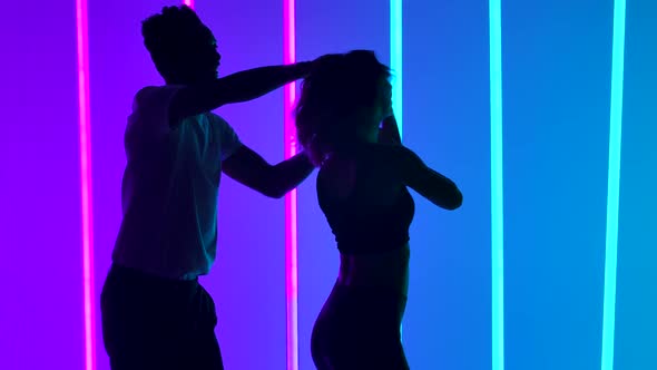 Professional Dancers Dancing Salsa in the Studio Against the Backdrop of Multicolored Neon Lights in