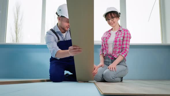 Man and Woman in Protective Helmets Check Locks of Laminate for Laying on Floor During Renovation