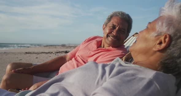 Happy senior hispanic couple relaxing on sunbeds on beach at sunset