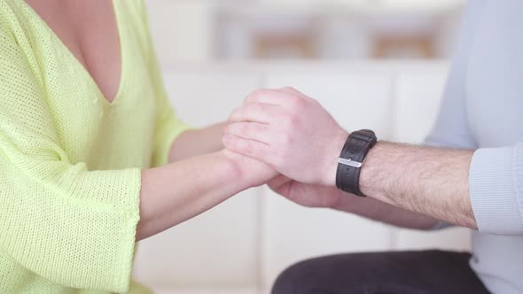 Unrecognizable Adult Man and Woman Holding Hands Sitting on Couch in Living Room