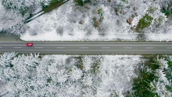 Aerial tracking of a red car which is driving through a wintry countryside street, straight from abo