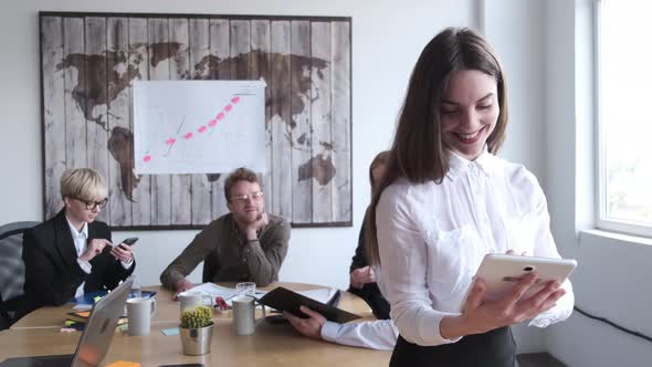 The Woman Is Standing with a Tablet in the Office with Collegues