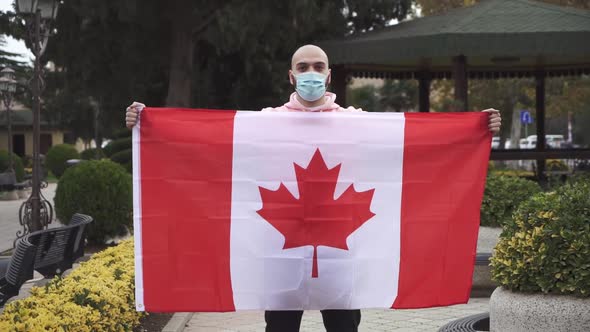 man with face mask holds Canadian flag