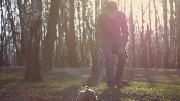 Man in Grey Coat and Mask Walks with Pedigreed Little Dog