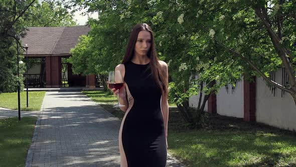 Elegant Woman with Glass of Wine Walking in Garden of Mansion