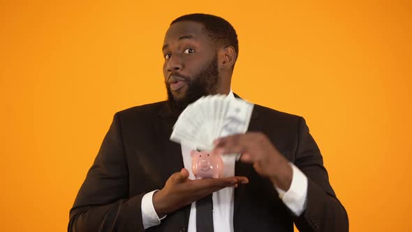 Cheerful African-American Man Holding Piggybank and Showing Dollar Cash, Deposit