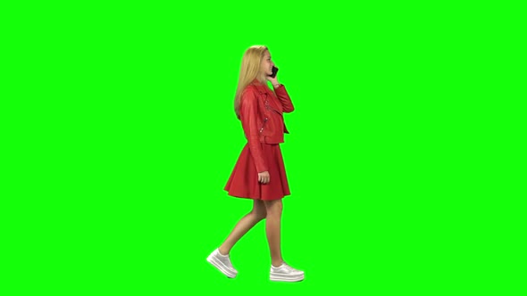 Blonde Girl Is Calmly Walking and Talking on the Mobile Phone at Green Screen. Chroma Key. Profile