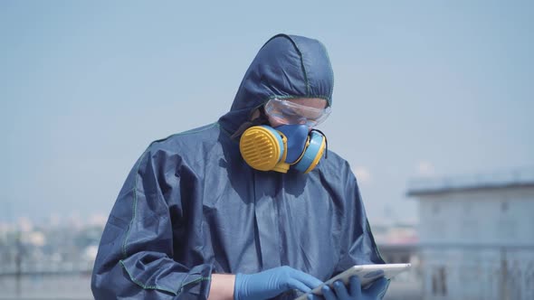 Portrait of Serious Man in Chemical Suit Using Tablet Outdoors. Young Confident Caucasian Specialist