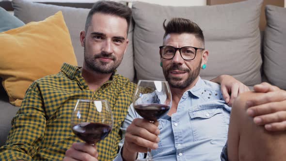 Gay Couple in Love Sitting at Home on the Floor and Toasting with Red Wine