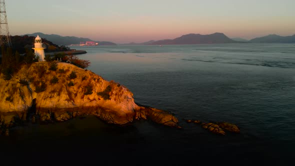 Aerial left rotating shot over Lighthouse facing Seto Island Sea with freighter passing by