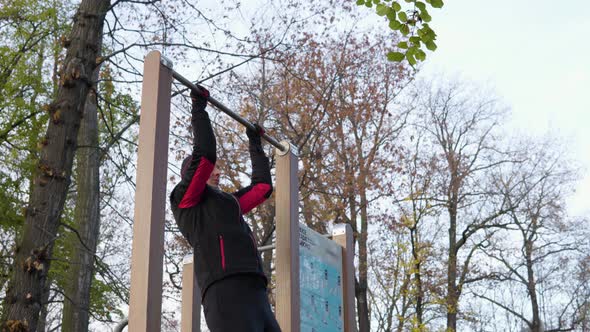 A Young Man Does Pull Ups in an Park on an Autumn Day