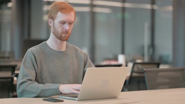 Young Man Looking at Camera While Using Laptop in Office
