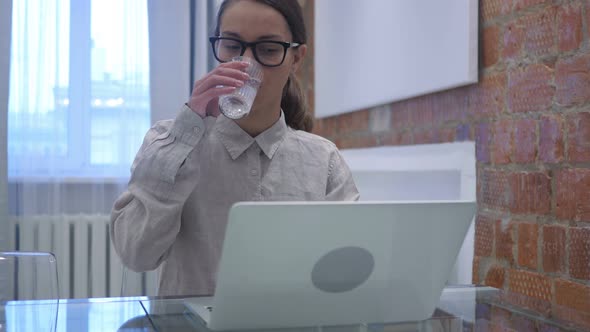 Hispanic Woman Drinking Water and Working on Laptop