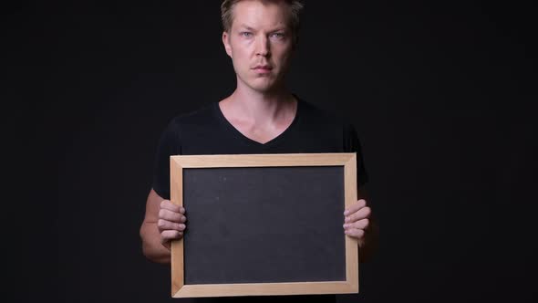 Young Handsome Man Holding Blackboard Against Black Background