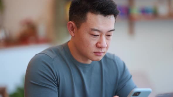 Concentrated Asian young man texting by phone
