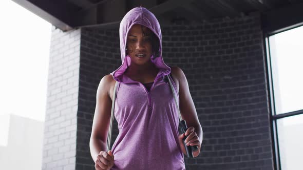 Portrait of african american woman holding skipping rope wearing hoodie looking at camera in an empt