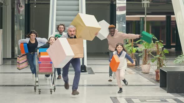 A Group of Contented Shopaholics with Shopping Bags and a Trolley Running Through the Mall