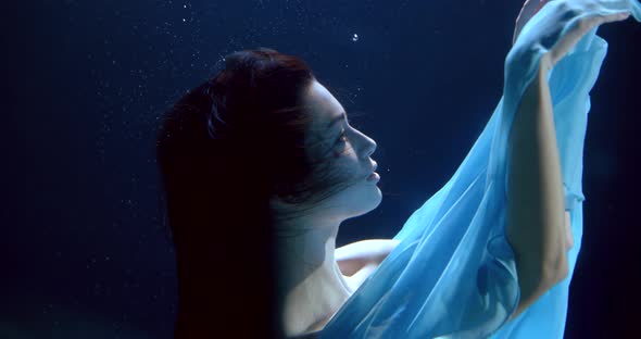 Portrait of a Cute Girl in Profile Under Water. She Moves Her Hands Beautifully with the Blue Cloth