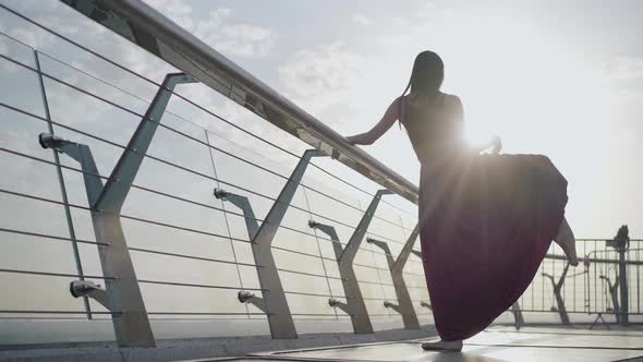 Back View Portrait of Caucasian Ballerina Raising Foot Up in Morning Sunrays, Wide Shot of Slim