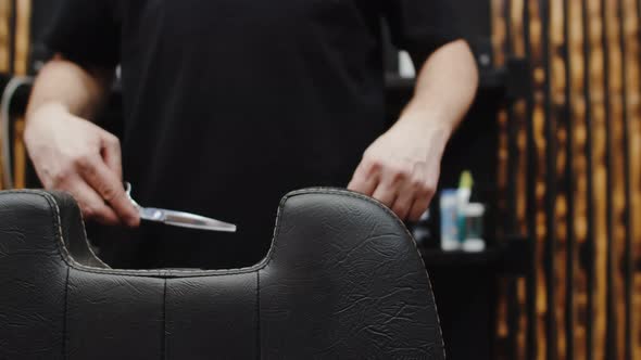 Male Barber's Hands with Scissors and Comb are Placed on a Barber Chair Closeup