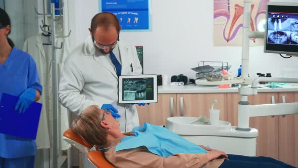Orthodontist in Gloves Holding Tablet Suggesting Treatment