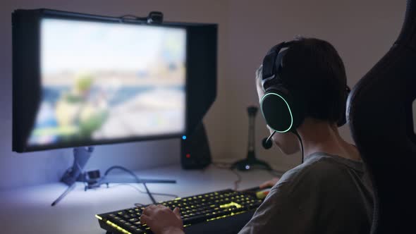 Young boy sitting in front of a computer, playing a game wearing a headset